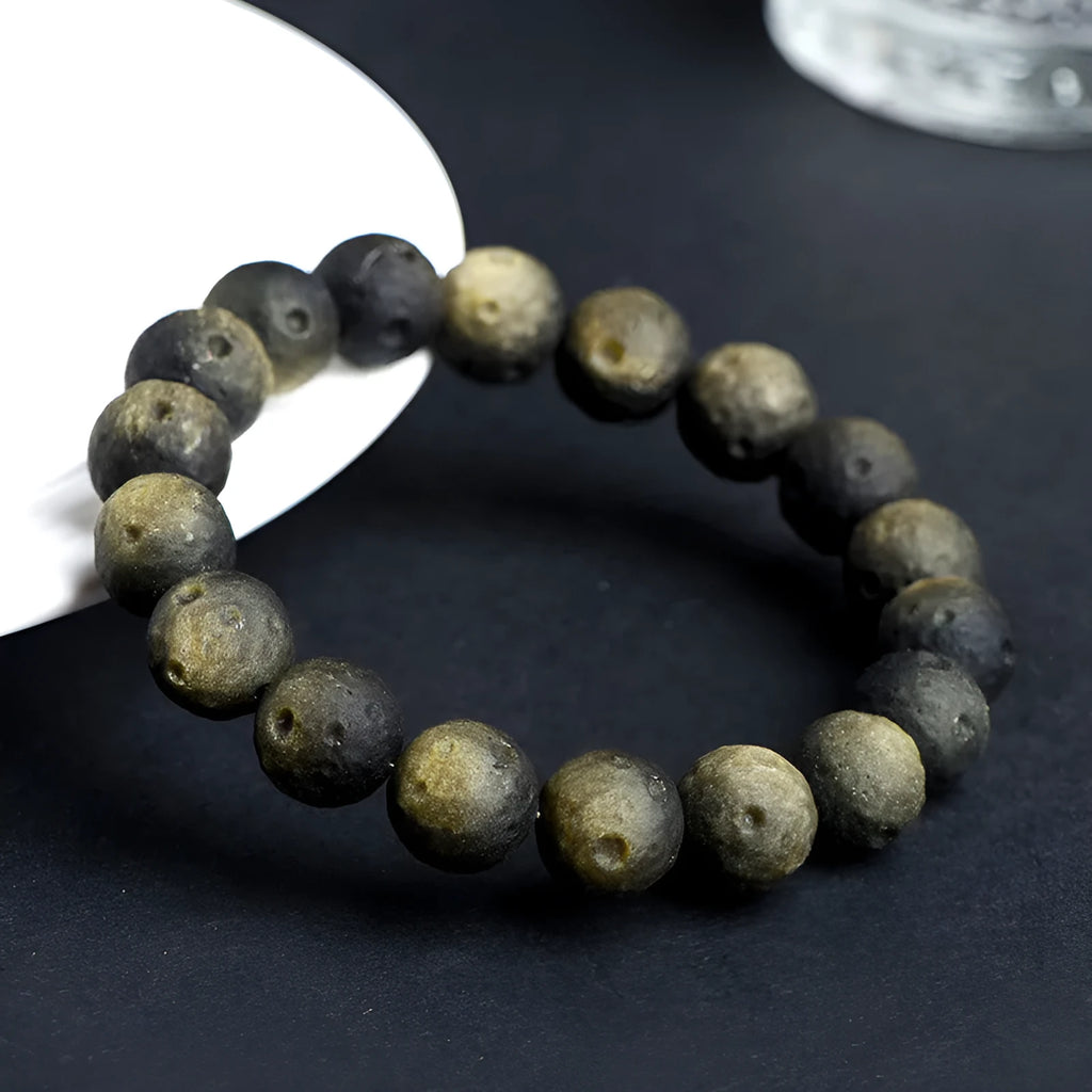 Natural obsidian crater ball bracelet showing textured beads in silver stone or golden obsidian colour on a wrist.