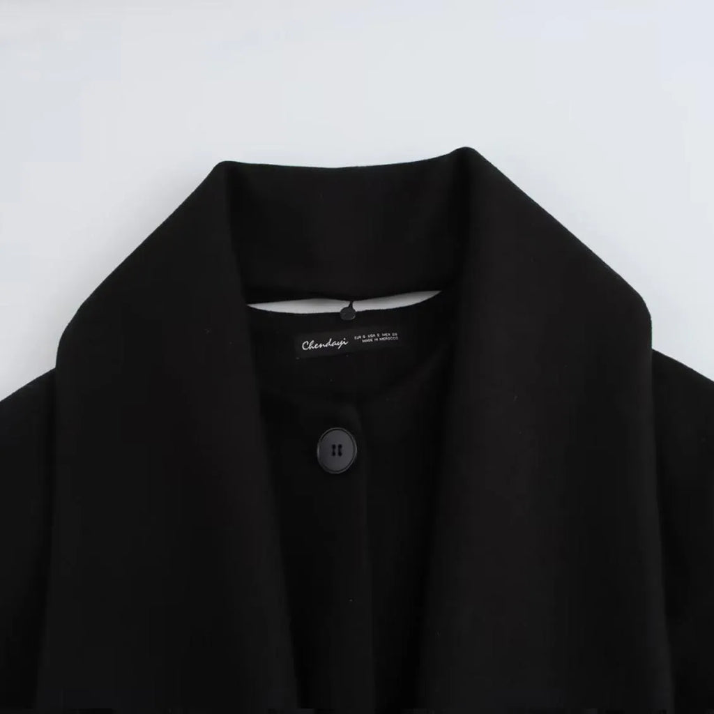 Women's long black overcoat with grey artificial fur collar, showing longline silhouette and pocket detail.
