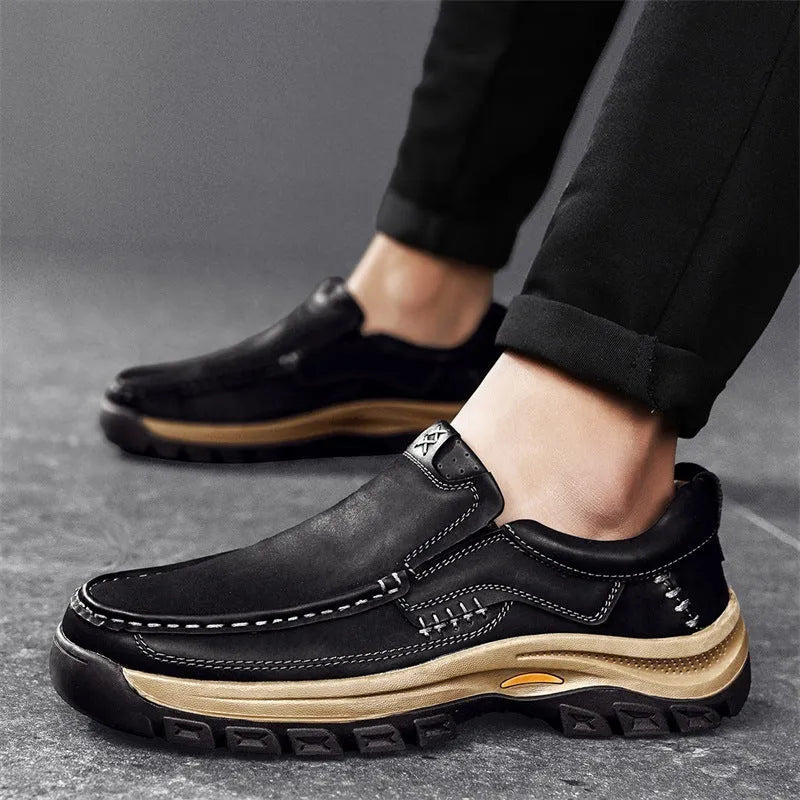 Men's black leather mountaineering shoes with thick rubber soles and round toe on a rocky path.