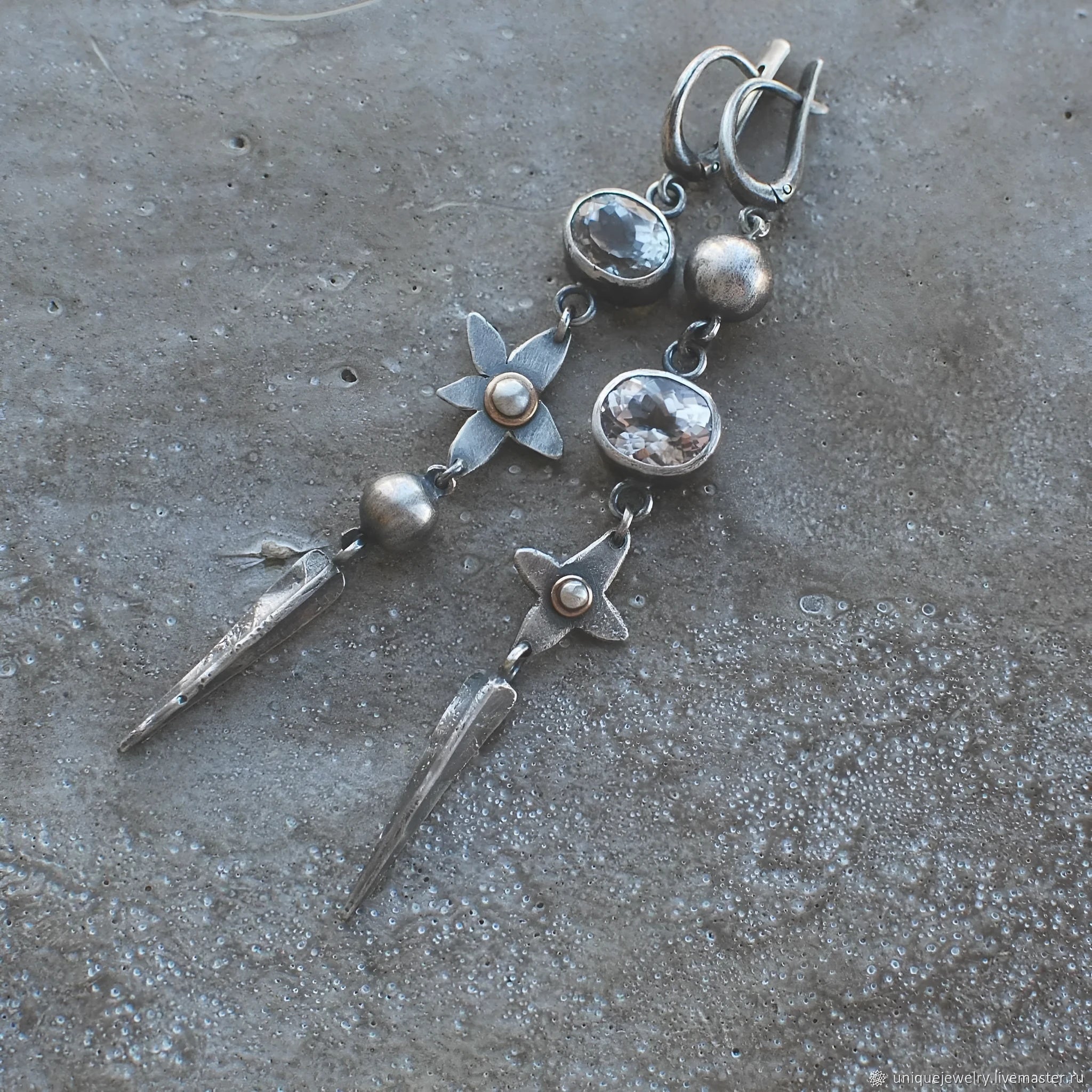 Pair of long geometric pendant earrings in antique silver with rhinestone detail on a white background.