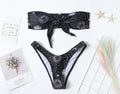 Black one-piece swimsuit with a bikini print pattern, featuring a split tube top and backless design.
