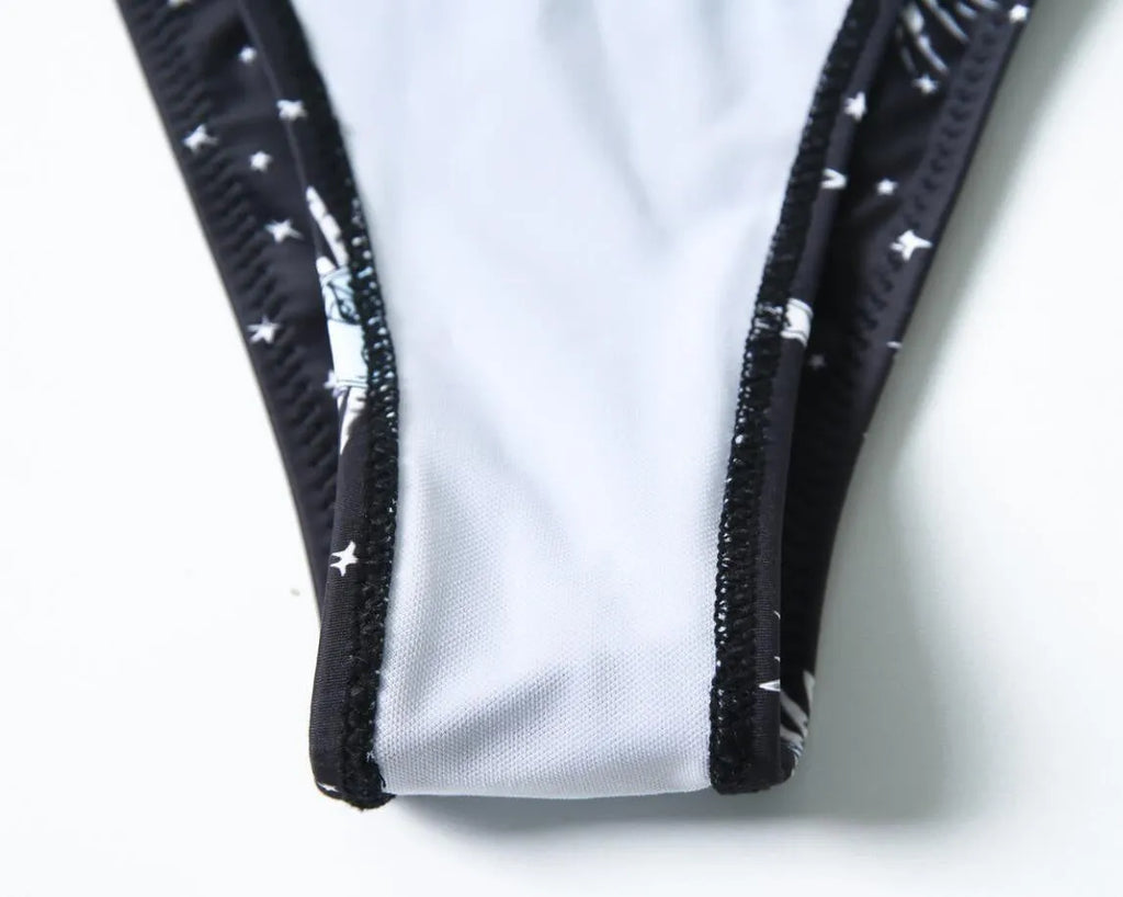 Black one-piece swimsuit with a bikini print pattern, featuring a split tube top and backless design.