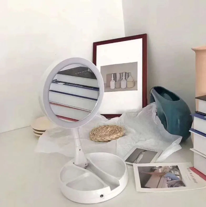 White foldable LED vanity mirror with USB charging port and double-sided storage compartment open on dressing table