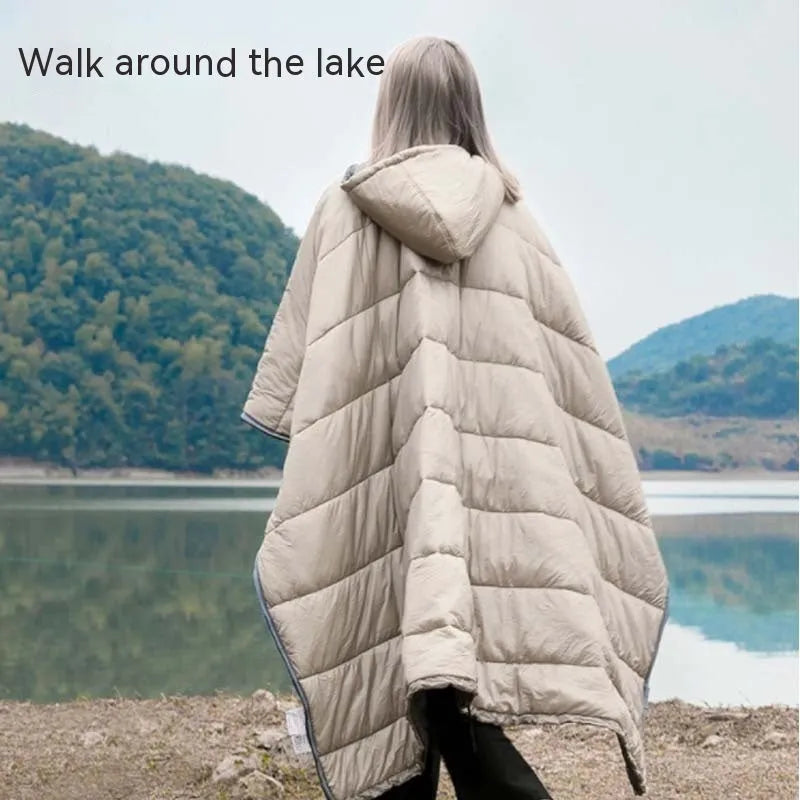 Adult wearing grey nylon cloak sleeping bag as wearable camping blanket outdoors