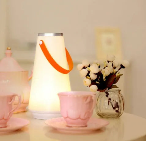 White rechargeable LED bedside table lamp with USB cable on a wooden surface.