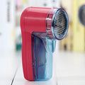 Compact blue portable electric lint remover for clothing on a grey sweater.