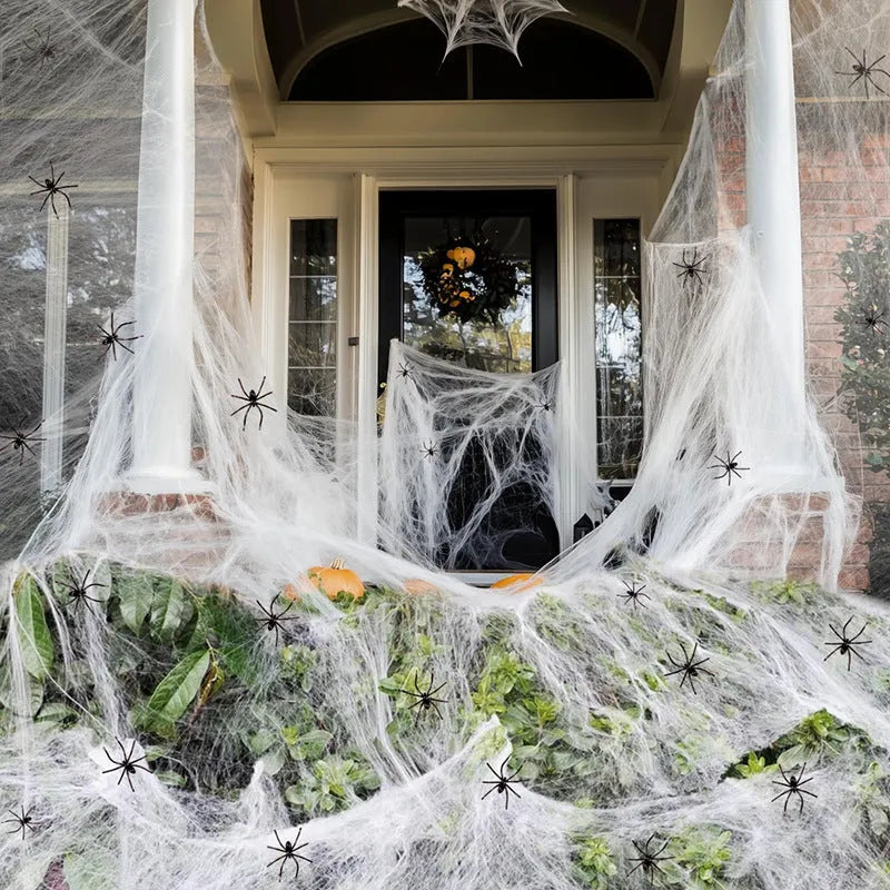White cotton spider web Halloween decoration with integrated synthetic spiders draped over fence