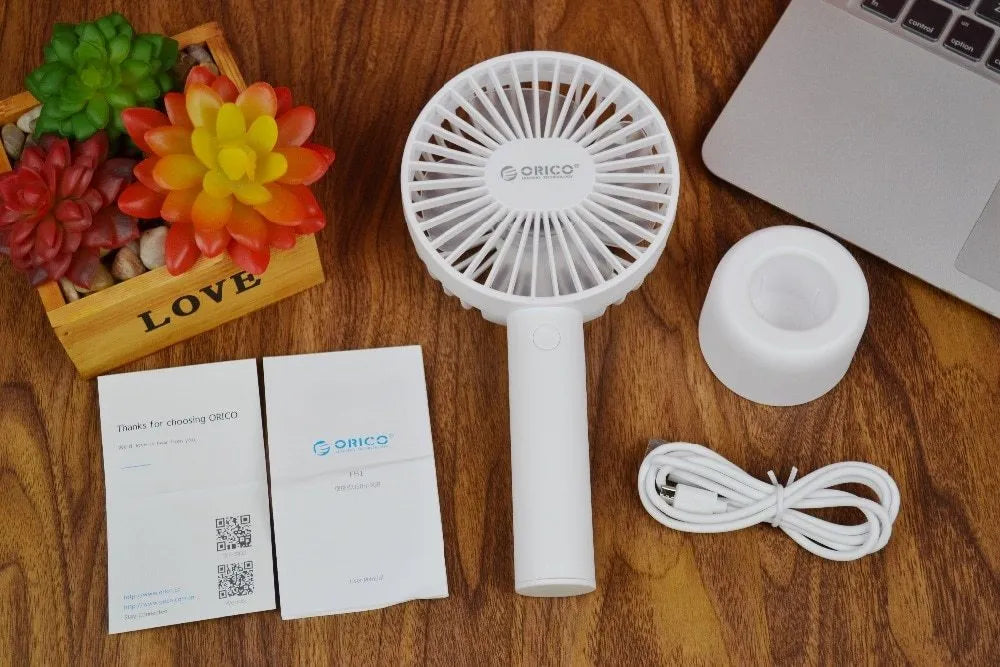 White ORICO FH1 portable USB rechargeable fan on a desk showing its compact size and three-speed button.
