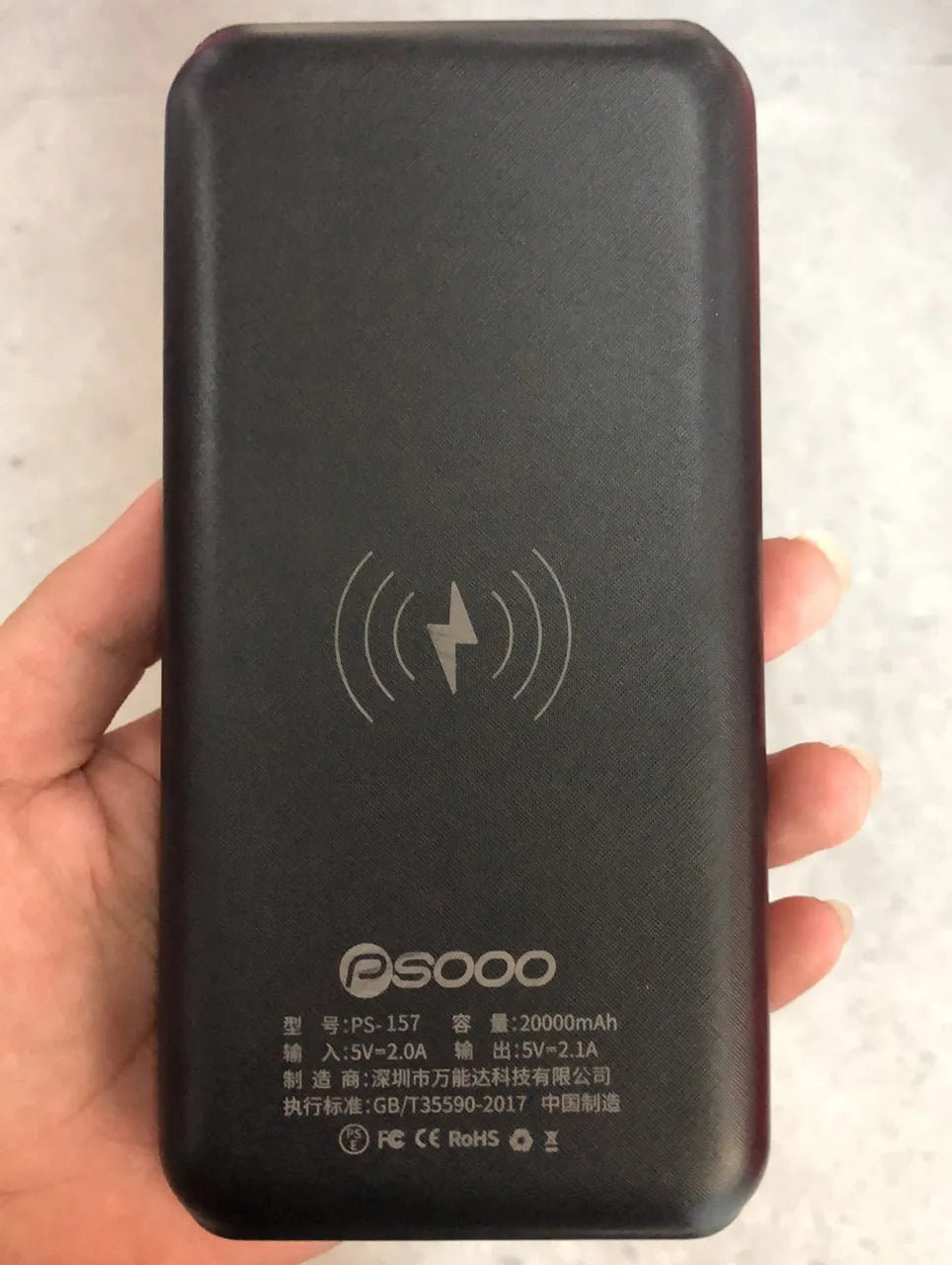 Black portable solar power bank with wireless charging pad and three USB ports on a wooden surface.