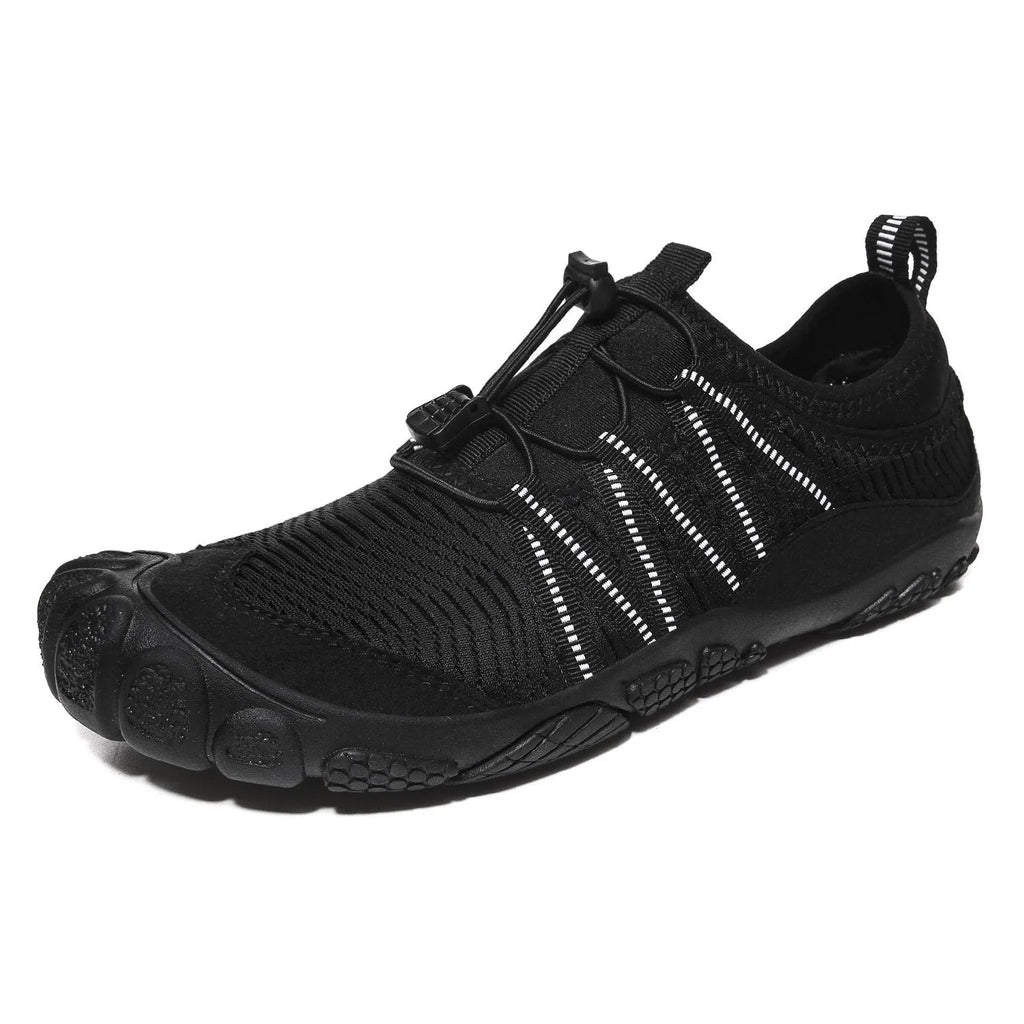 Unisex outdoor water shoes in black with mesh upper and rubber sole, shown on rocky riverbank.