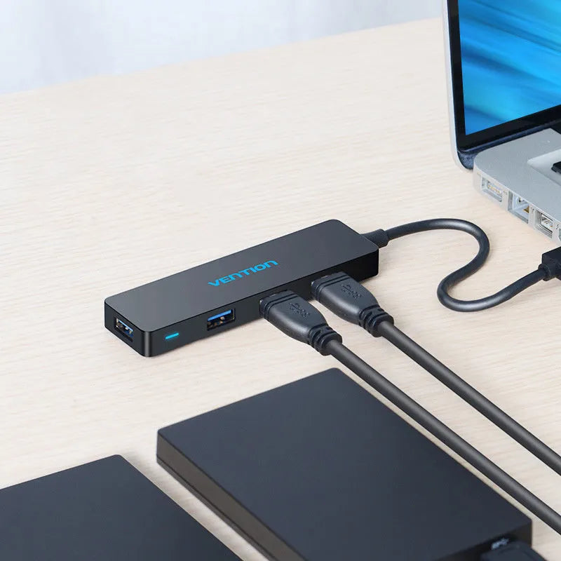 Black USB 3.0 hub with four ports and a short cable on a desk