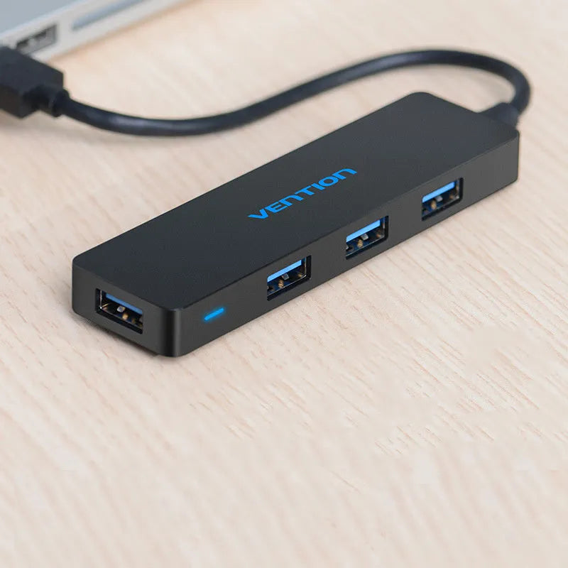 Black USB 3.0 hub with four ports and a short cable on a desk