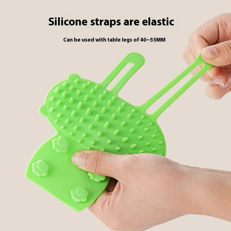 Silicone cat grooming comb with adjustable strap attached to furniture leg for scratching and hair removal