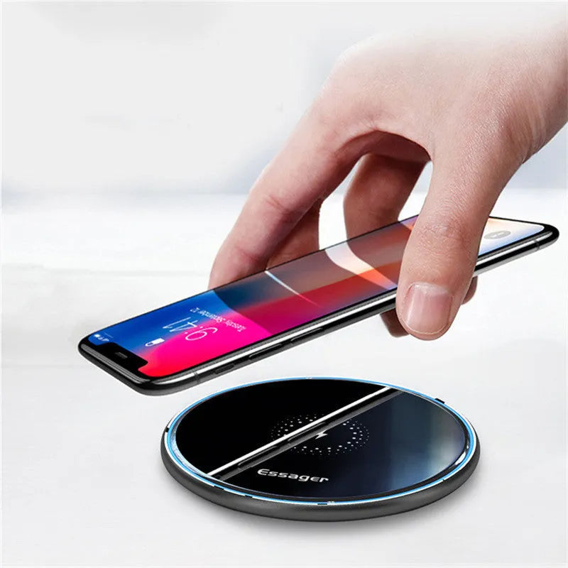 Black wireless charging pad on desk with phone charging, showing blue LED indicator light