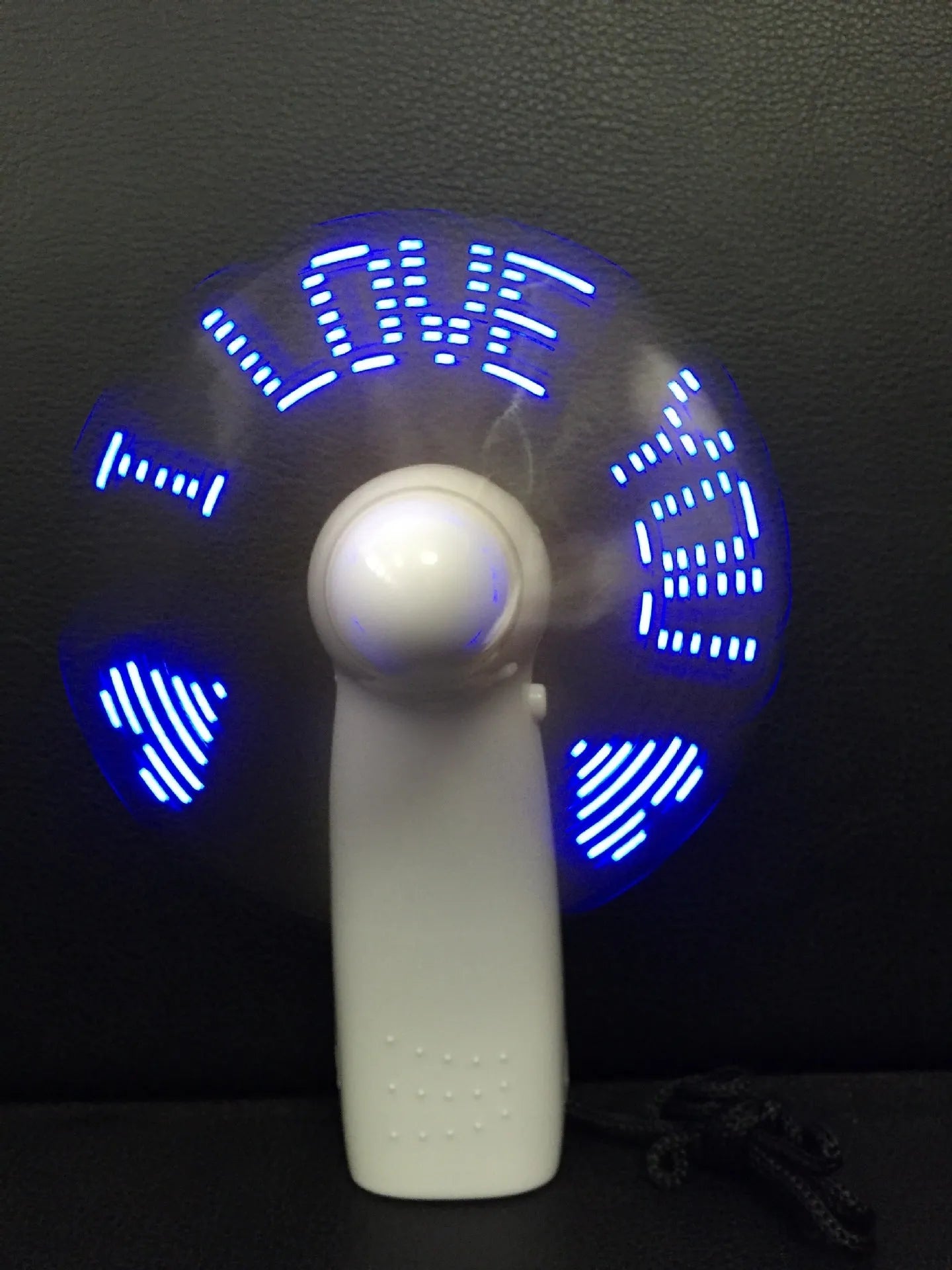White handheld mini fan showing blue and red LED 'I Love You' pattern, held in hand.
