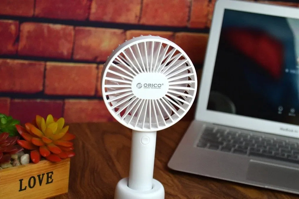 White ORICO FH1 portable USB rechargeable fan on a desk showing its compact size and three-speed button.