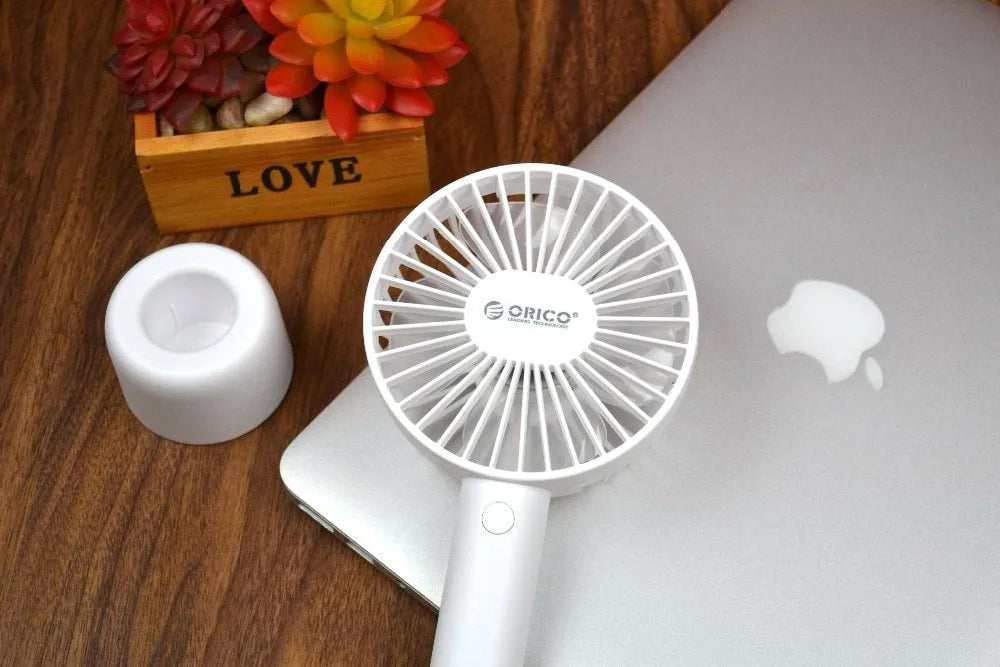 White ORICO FH1 portable USB rechargeable fan on a desk showing its compact size and three-speed button.