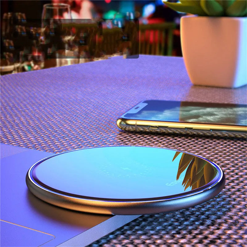Black wireless charging pad on desk with phone charging, showing blue LED indicator light