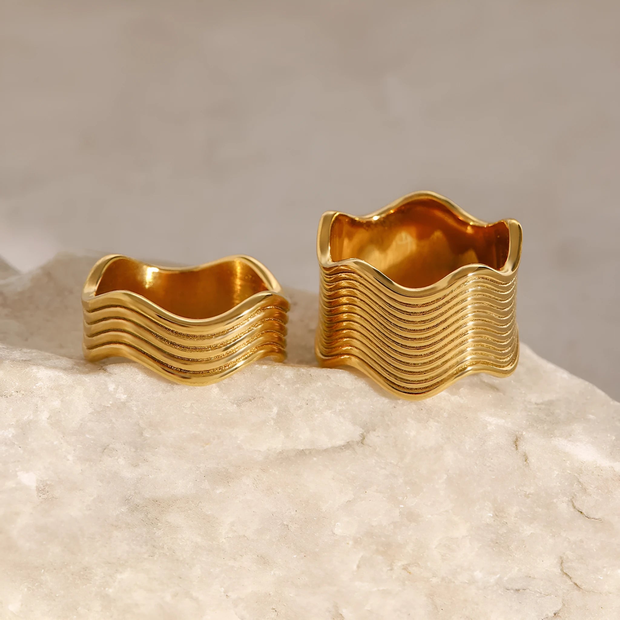 Close-up of a stainless steel ring with a wide geometric wave pattern on a white background.