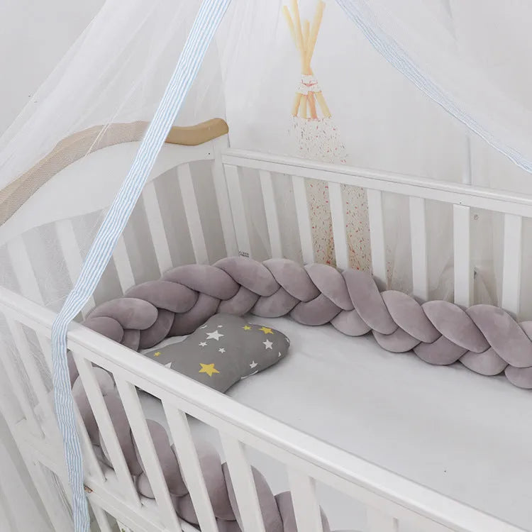Flexible braided cot bumper made of soft spandex velvet, shown in a light grey colour wrapped around a crib.