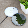 Black wireless charging pad on desk with phone charging, showing blue LED indicator light