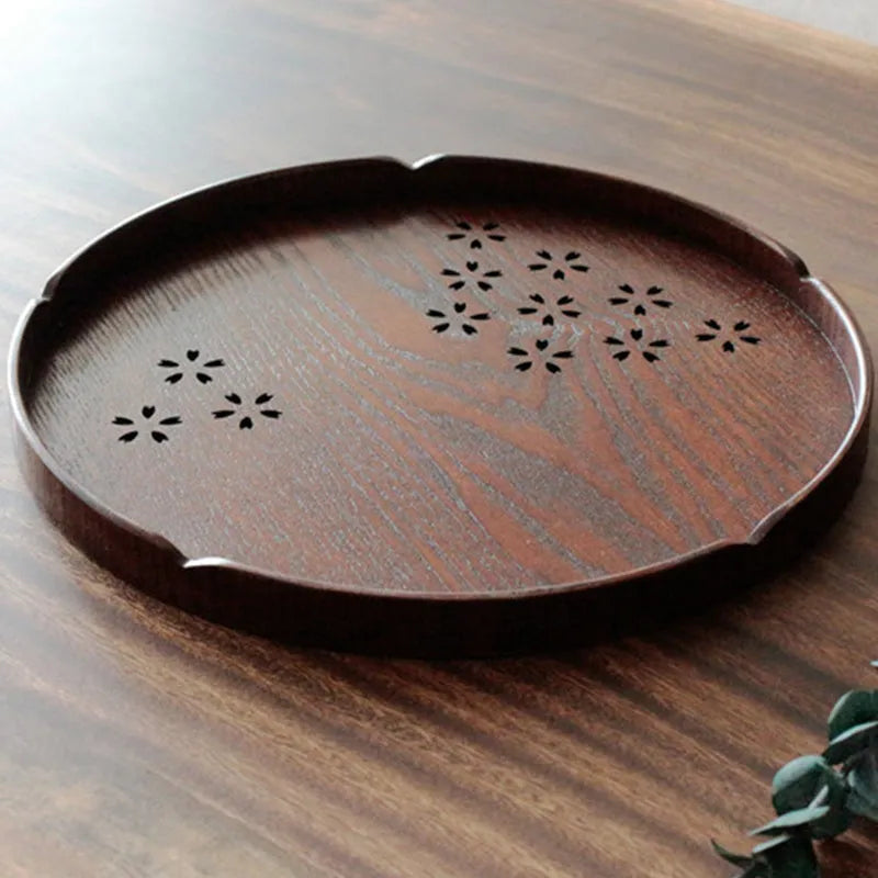 Twelve wooden dessert plates with carved cherry blossom design arranged in storage tray