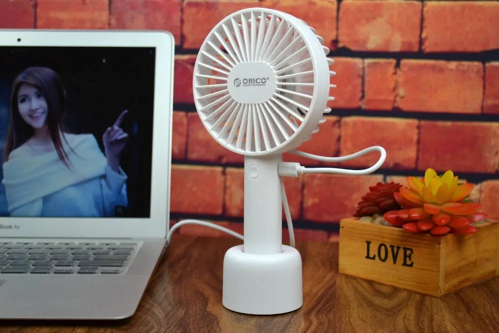 White ORICO FH1 portable USB rechargeable fan on a desk showing its compact size and three-speed button.