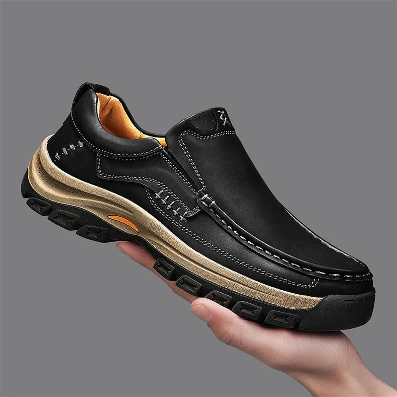 Men's black leather mountaineering shoes with thick rubber soles and round toe on a rocky path.
