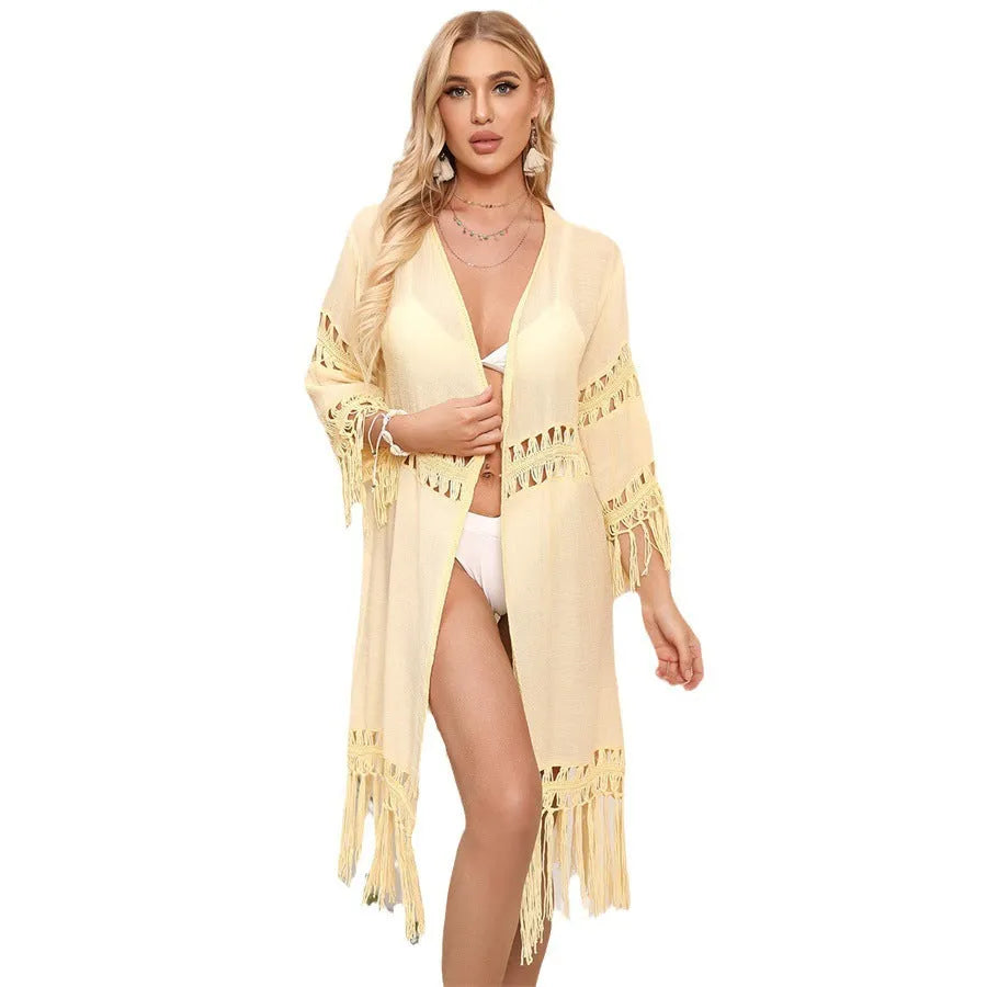 Women's yellow hand-crocheted beach cover-up cardigan with tassel trim on a hanger.