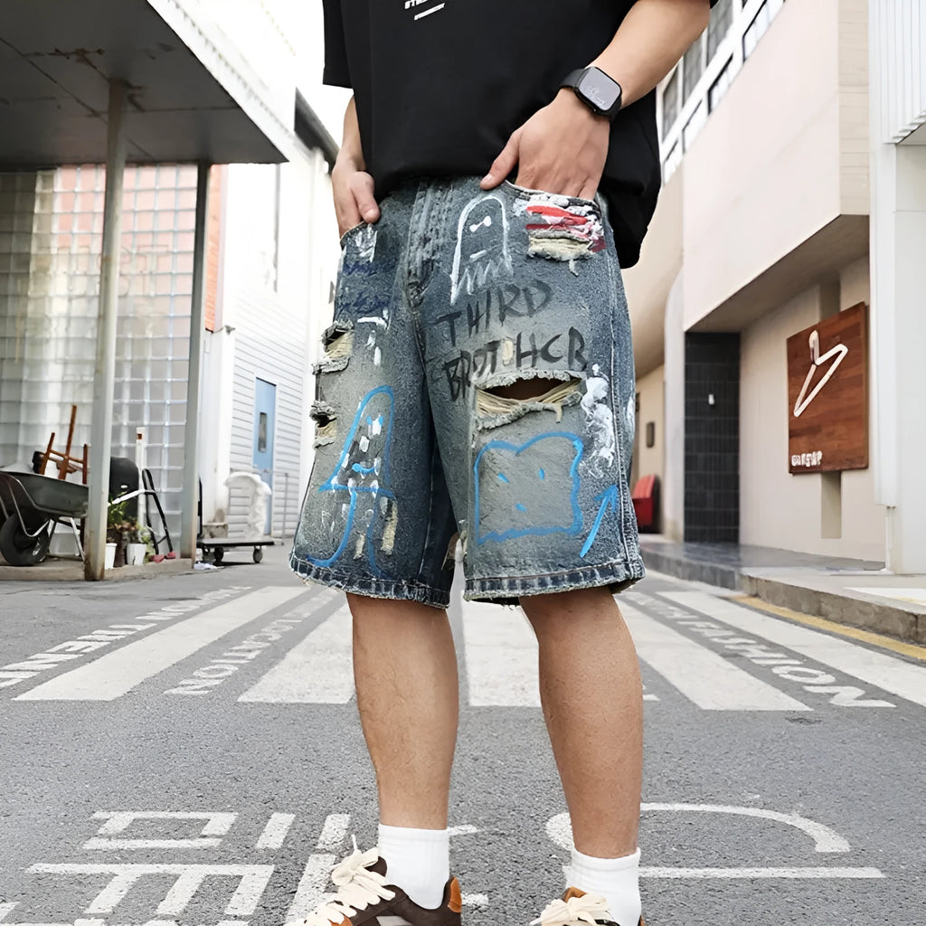 Blue men's denim shorts with ripped knees and graffiti图案, featuring a straight leg and zipper fly.