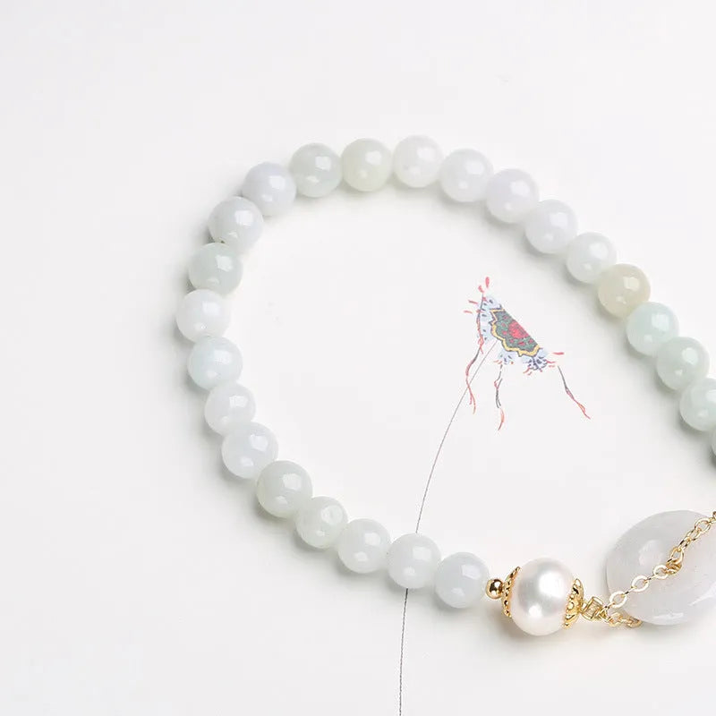 Close-up of a women's pearl bracelet with a natural emerald peace buckle charm and a jade round pendant.