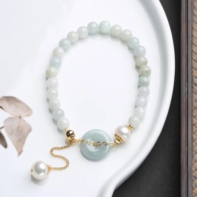 Close-up of a women's pearl bracelet with a natural emerald peace buckle charm and a jade round pendant.