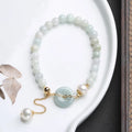 Close-up of a women's pearl bracelet with a natural emerald peace buckle charm and a jade round pendant.