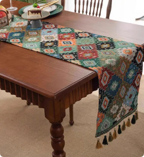 Long European-style retro table runner with decorative tassels in a floral design on a wooden table.