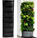 Vertical green felt wall hanging planter with multiple pockets full of herbs and flowers