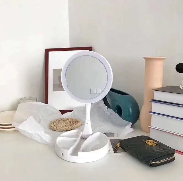 White foldable LED vanity mirror with USB charging port and double-sided storage compartment open on dressing table