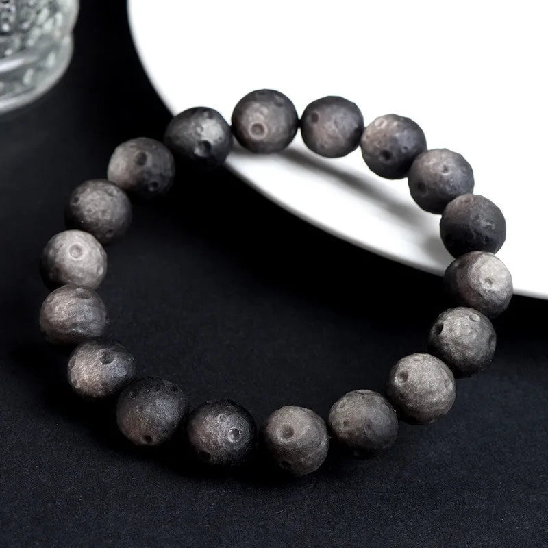 Natural obsidian crater ball bracelet showing textured beads in silver stone or golden obsidian colour on a wrist.