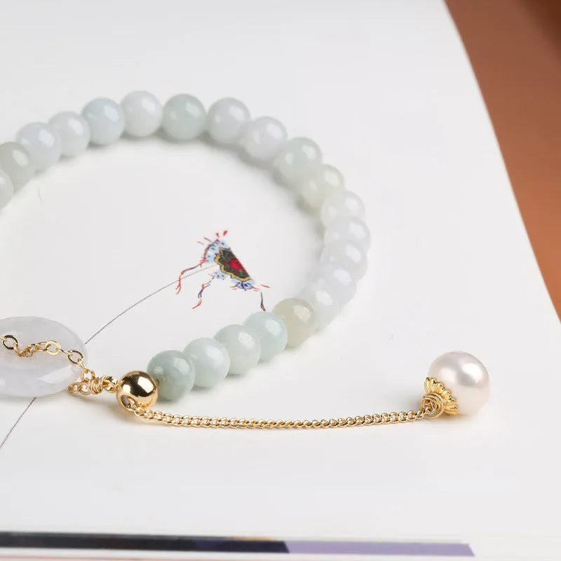 Close-up of a women's pearl bracelet with a natural emerald peace buckle charm and a jade round pendant.