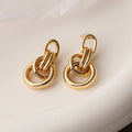 A pair of gold-colour geometric earrings with an irregular, high-profile design on a white background.