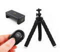 Black flexible octopus leg tripod standing on a table next to a smartphone