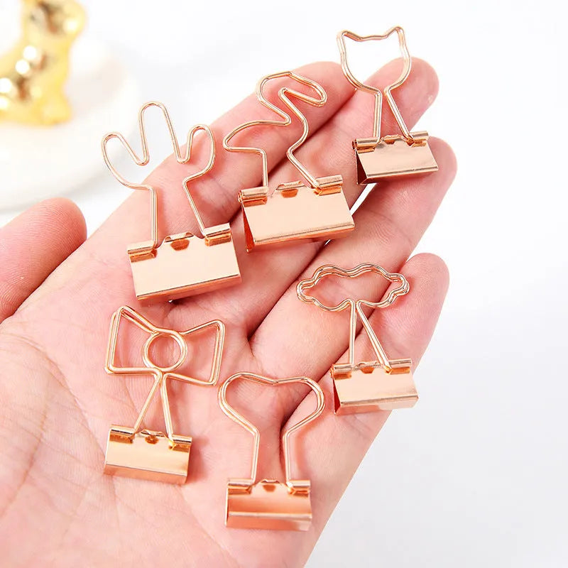 Small gold-plated decorative metal clip with long-tail design, showing optional flamingo, love, clouds, cat, cactus, and bow motifs.