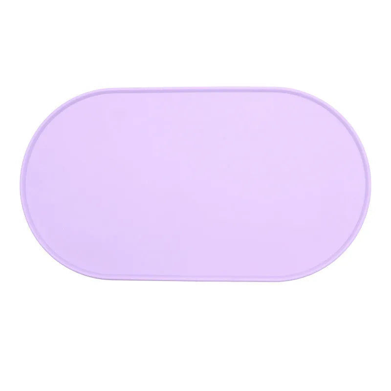 Green silicone placemat for cat bowls on a wooden floor.