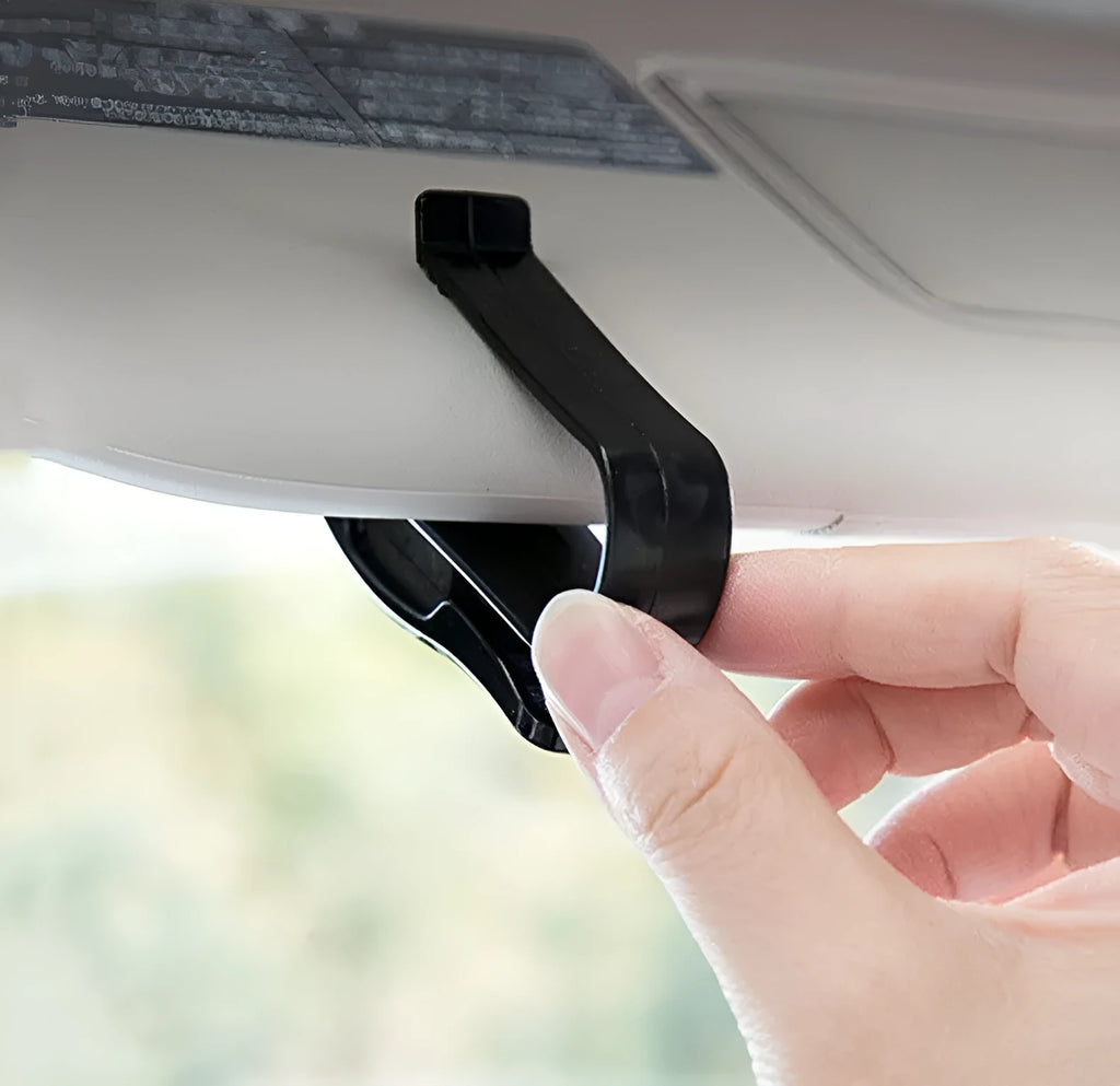 Black plastic multifunctional car mounted glasses and card clip attached to a sun visor holding sunglasses and an ID card