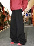 Man wearing straight-leg pleated trousers in a cotton-polyester blend, available in black, brown, and apricot.