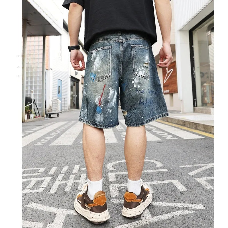 Blue men's denim shorts with ripped knees and graffiti图案, featuring a straight leg and zipper fly.
