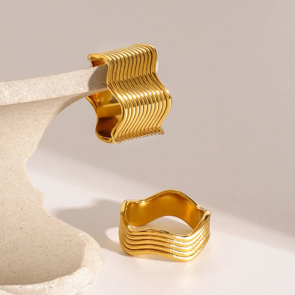 Close-up of a stainless steel ring with a wide geometric wave pattern on a white background.