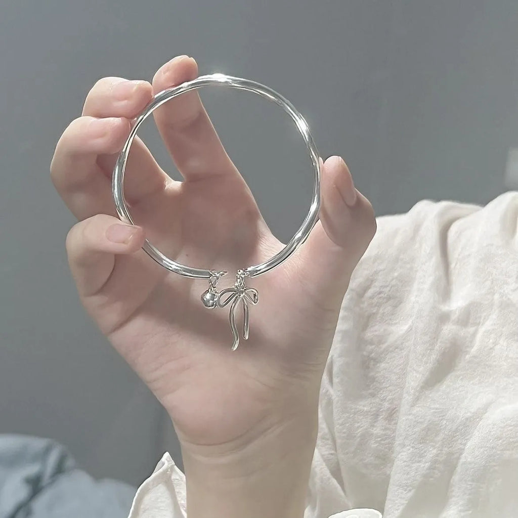Silver adjustable bracelet with a detailed bow charm and bell opening.