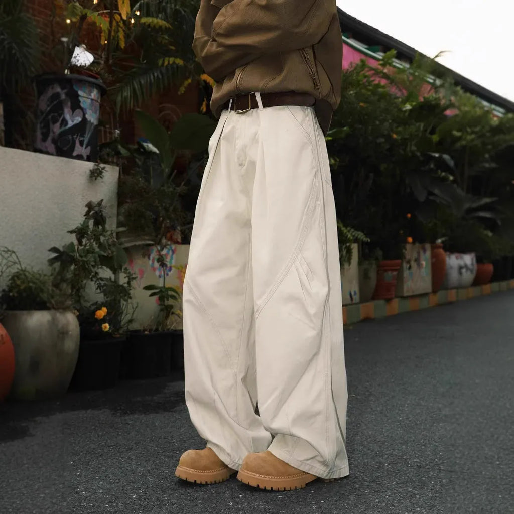 Man wearing straight-leg pleated trousers in a cotton-polyester blend, available in black, brown, and apricot.