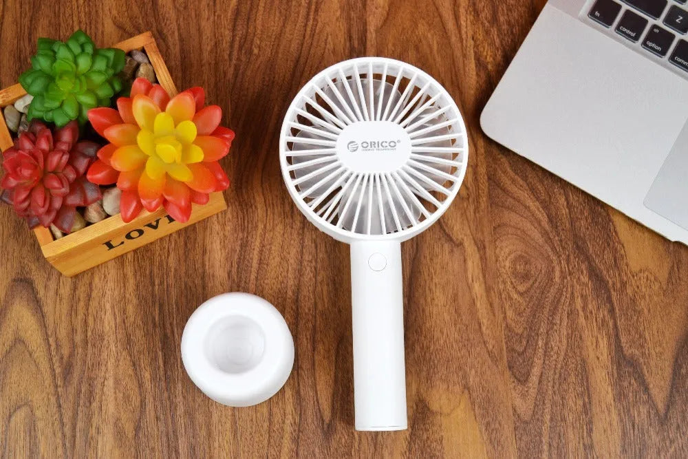 White ORICO FH1 portable USB rechargeable fan on a desk showing its compact size and three-speed button.