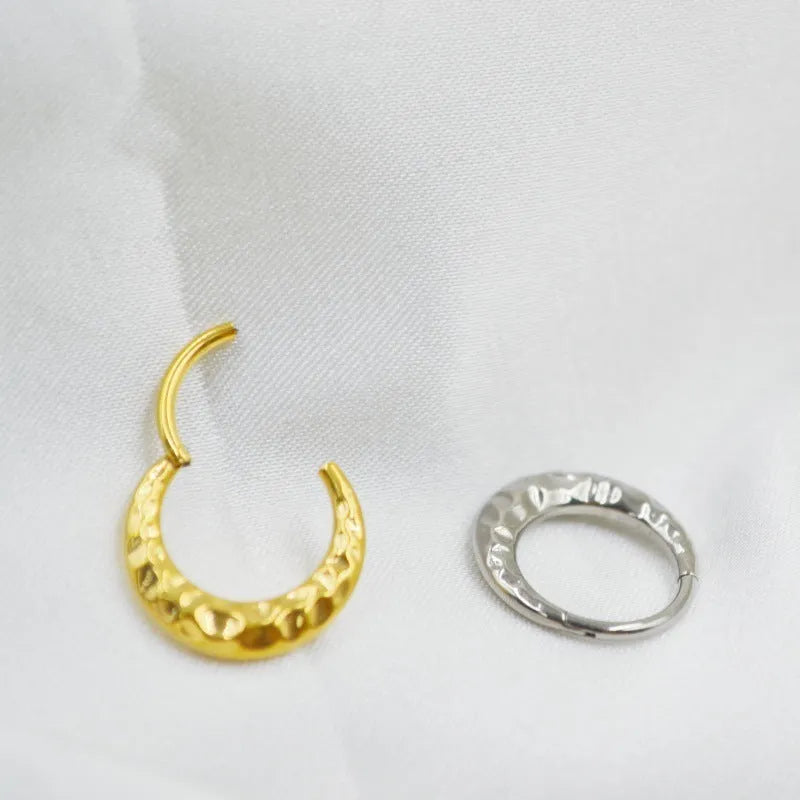 Close-up of a carved concave-convex titanium nose ring in gold finish, showing textured surface.